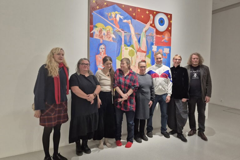 Kahdeksan taiteilijaa maalauksen edessä.