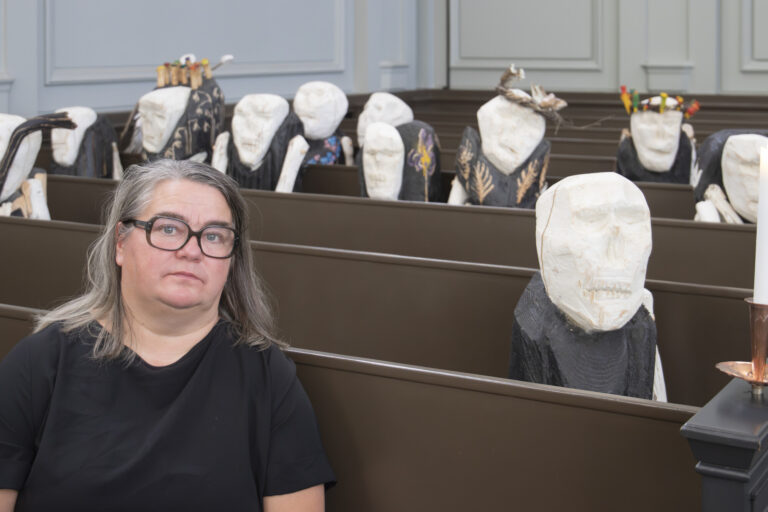 Reetta Gröhn-Soininen istuu kirkon penkissä, taustalla näkyy hänen veistoksiaan.