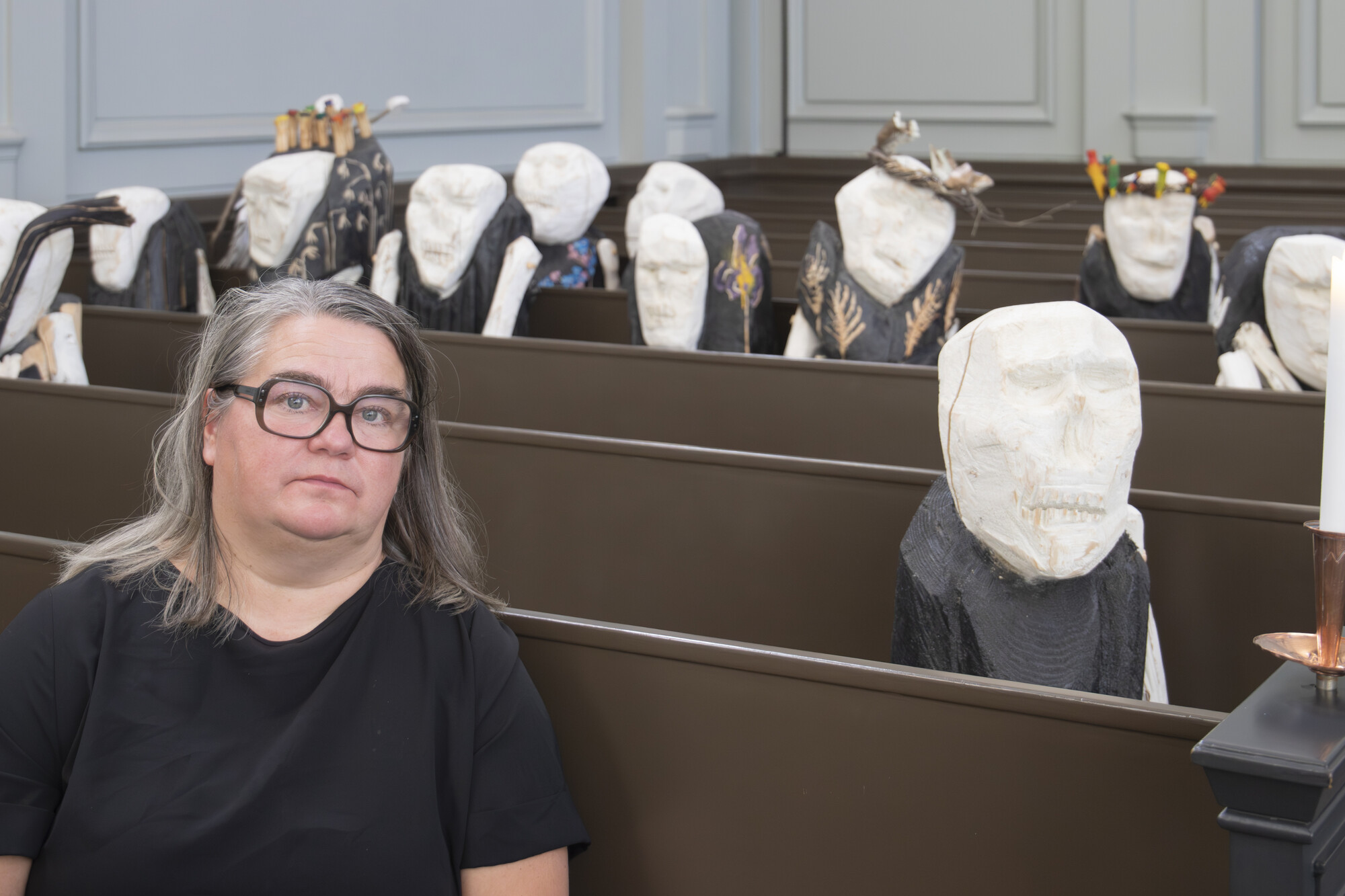 Reetta Gröhn-Soininen istuu kirkon penkissä, taustalla näkyy hänen veistoksiaan.