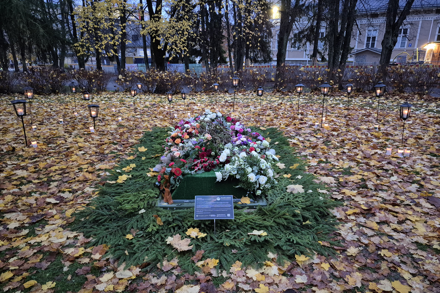 Hautaa muistuttava kumpu, jonka päällä on kukkia, ympärllä lyhtyjä.